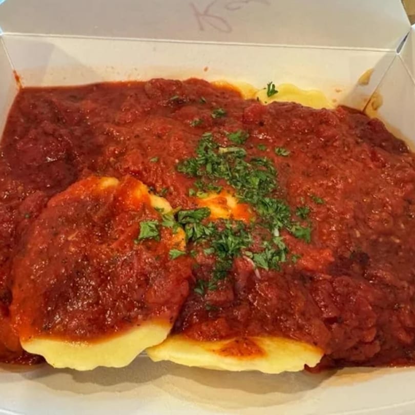 Evangelo's ravioli with rich red tomato sauce and fresh green parsley in a takeout container.